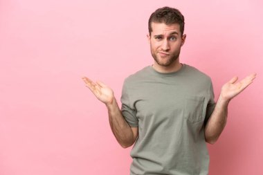 Pembe arka planda izole edilmiş genç beyaz adam ellerini kaldırırken şüpheleri var.