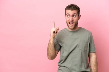 Pembe arka planda izole edilmiş genç beyaz adam çözümü bulmak için parmağını kaldırıyor.