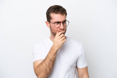 Beyaz arka planda gözlüklü ve şüpheleri olan beyaz tenli genç bir adam.