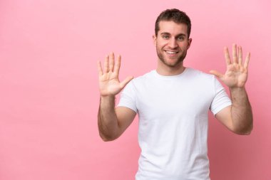 Pembe arka planda izole edilmiş genç beyaz adam parmaklarıyla ona kadar sayıyor.