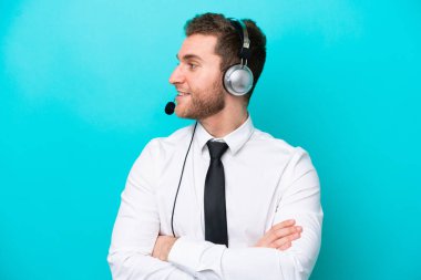 Telemarketer caucasian man working with a headset isolated on blue background looking side