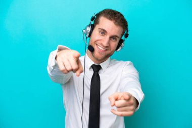 Tele pazarlamacı beyaz bir adam mavi arka planda izole edilmiş bir kulaklıkla çalışıyor.