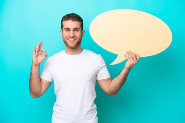 Beyaz, mavi arka planda izole edilmiş genç bir adam elinde boş bir konuşma balonu tutuyor ve 