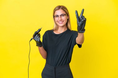 Dövme sanatçısı Uruguaylı kadın sarı arka planda izole edilmiş gülümsüyor ve zafer işareti gösteriyor