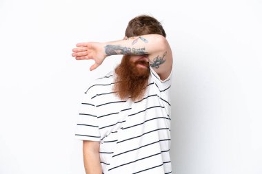 Kızıl saçlı, sakallı bir adam beyaz arka planda, gözleri elleriyle kapatıyor.