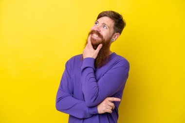 Sarı arka planda sakallı kızıl saçlı adam gülümserken yukarı bakıyor.