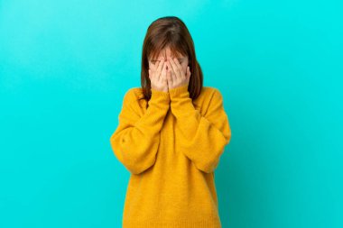 Kızıl saçlı kız mavi arka planda izole edilmiş, yorgun ve hasta bir ifadeyle.