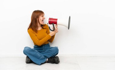 Kızıl saçlı kız, beyaz arka planda izole bir şekilde yerde oturmuş megafonla bağırıyor.