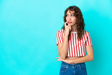 Kıvırcık saçlı genç kadın mavi arka planda izole edilmiş gergin ve korkmuş.