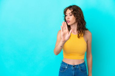 Mavi arka planda, kıvırcık saçlı genç bir kadın dur hareketi yapıyor ve hayal kırıklığına uğruyor.