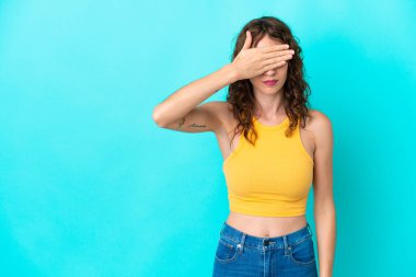 Mavi arka planda izole edilmiş kıvırcık saçlı genç bir kadın gözlerini elleriyle kapatıyor. Bir şey görmek istemiyorum.