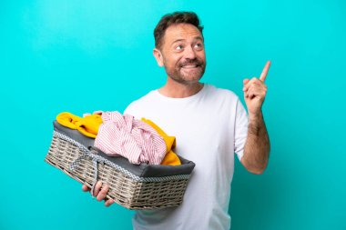 Mavi arka planda izole edilmiş çamaşır sepetini tutan orta yaşlı kadın harika bir fikre işaret ediyor.