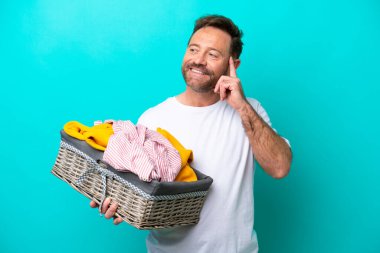 Mavi arka planda bir çamaşır sepetini tutan orta yaşlı kadın yukarı bakarken bir fikir düşünüyor.