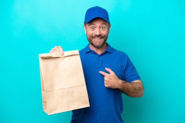 Orta yaşlı bir adam mavi arka planda izole edilmiş bir paket yiyecek alıyor.