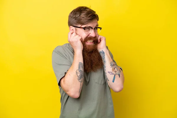 Redhead man with beard isolated on yellow background frustrated and covering ears