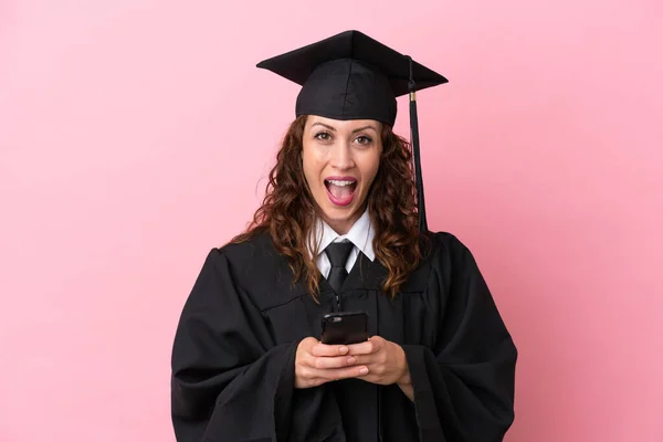 Young university graduate woman isolated on pink background surprised and sending a message