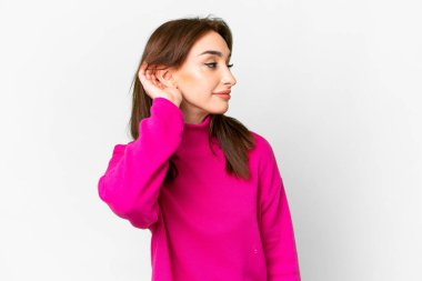 İzole edilmiş beyaz arka planda genç beyaz kadın elini kulağına koyarak bir şeyler dinliyor.