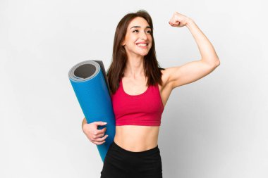 Genç beyaz kadın yoga derslerine giderken izole edilmiş beyaz arka planda bir minder tutuyor ve zaferi kutluyor.