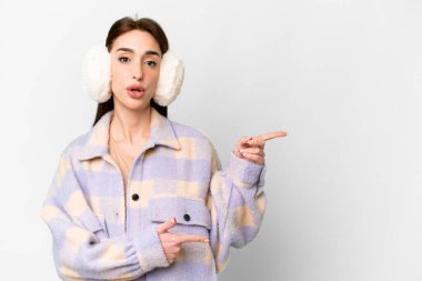 İzole edilmiş beyaz arka plan üzerinde kışlık kuklalar takan genç beyaz kadın şaşırmış ve işaret ediyor.