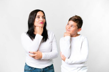 Kafkasyalı küçük bir çocuk, annesi izole edilmiş beyaz bir arka planda duruyor ve bir fikir düşünüyor.