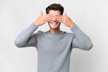 İzole edilmiş beyaz arka planda genç, yakışıklı beyaz bir adam. Gözlerini elleriyle kapatıyor.