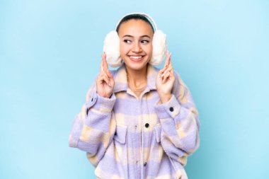 Mavi arka planda izole edilmiş kışlık kuklalar takan genç bir Arap kadın.