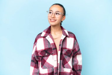 Genç bir Arap kadın mavi arka planda izole edilmiş bir şekilde yukarı bakarken bir fikir düşünüyor.