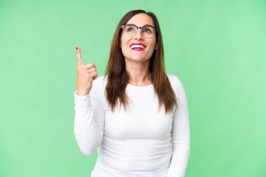 Orta yaşlı kadın izole edilmiş krom anahtar arka planı yukarı işaret ediyor ve şaşırdı