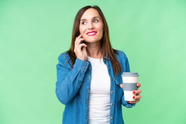 Orta yaşlı bir kadın izole edilmiş krom anahtar geçmişi var. Elinde kahve ve cep telefonu var.