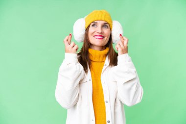 Orta yaşlı bir kadın, izole edilmiş krom anahtar arkaplan üzerinde kış manşeti takıyor ve parmaklarını çapraz yapıyor.