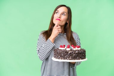 Orta yaşlı beyaz kadın izole edilmiş krom anahtar arka planda doğum günü pastası tutuyor ve