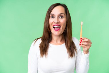 Orta yaşlı bir kadın, izole edilmiş krom anahtar arka planda dişlerini fırçalıyor. Şaşırtıcı ve şok edici bir yüz ifadesi var.