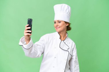 Orta yaşlı aşçı kadın izole bir arka planda selfie çekiyor.