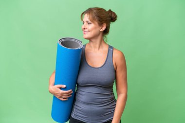 Orta yaşlı sporcu bir kadın yoga derslerine giderken arka planda izole edilmiş arka planda bir minder tutuyor.