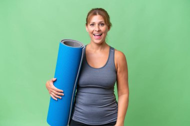 Orta yaşlı sporcu bir kadın yoga derslerine giderken elinde paspas tutarken yüzünde sürpriz bir ifade oluyor.