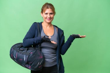 Spor çantasıyla orta yaşlı bir kadın izole edilmiş arka planda. Davet etmek için ellerini yana uzatıyor.