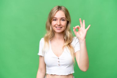 Tecrit edilmiş arka planda genç bir İngiliz kadın parmaklarıyla tamam işareti gösteriyor.