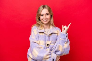 Kırmızı arka planda izole edilmiş genç bir İngiliz kadın mutlu ve yukarıya bakıyor.