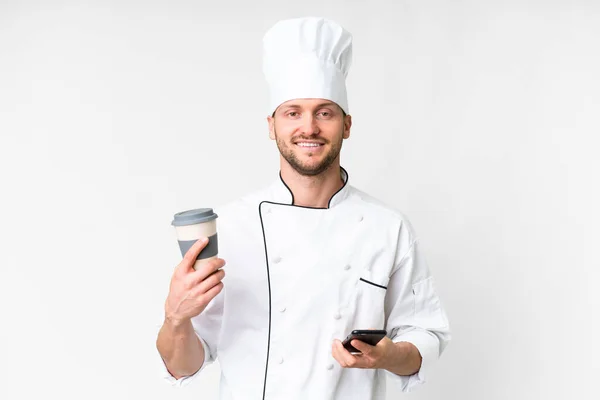 年轻的高加索厨师站在与世隔绝的白色背景上 手里拿着咖啡和手机 — 图库照片