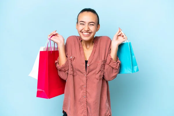 Young Arab woman isolated on blue background holding shopping bags and smiling