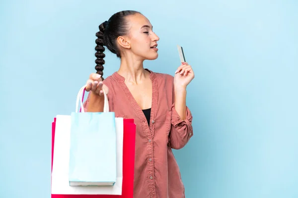 Young Arab woman isolated on blue background holding shopping bags and a credit card