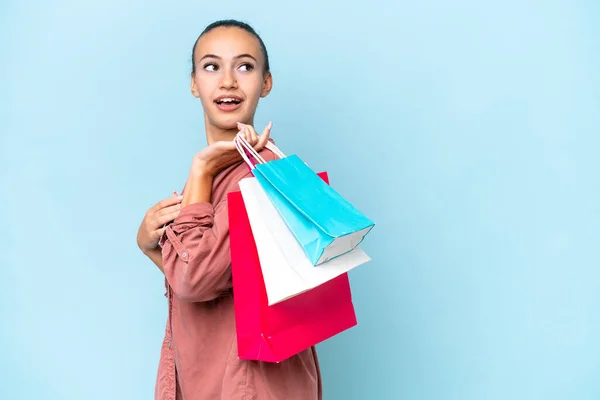 Young Arab woman isolated on blue background holding shopping bags and looking back