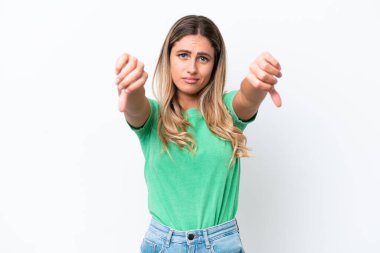 Genç Uruguaylı kadın beyaz arka planda izole edilmiş, baş parmağını iki eliyle aşağı gösteriyor.