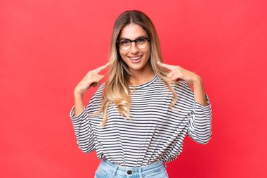 Genç Uruguaylı kadın kırmızı arka planda izole edilmiş bir şekilde baş parmak işareti yapıyor.
