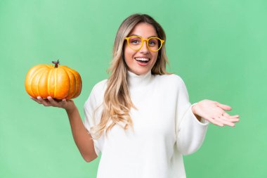 Genç Uruguaylı kadın balkabağını izole edilmiş arka planda tutuyor ve şok olmuş bir yüz ifadesi var.