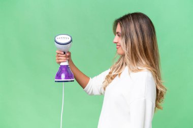 Genç Uruguaylı kadın, izole edilmiş arka planda mutlu bir ifadeyle bir ütü tutuyor.