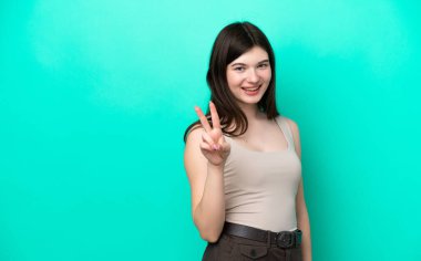 Yeşil arka planda izole edilmiş genç Rus kadın gülümsüyor ve zafer işareti gösteriyor.