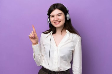 Mor arka planda izole edilmiş bir kulaklıkla çalışan pazarlamacı Rus kadın en iyinin işareti olarak parmağını kaldırıyor.