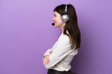 Tele pazarlamacı Rus kadın. Kulaklıkla çalışıyor. Mor arka planda, yanal pozisyonda.