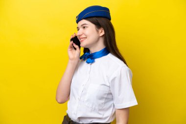 Uçak hostesi Rus kadın, sarı arka planda izole edilmiş cep telefonuyla biriyle sohbet ediyor.